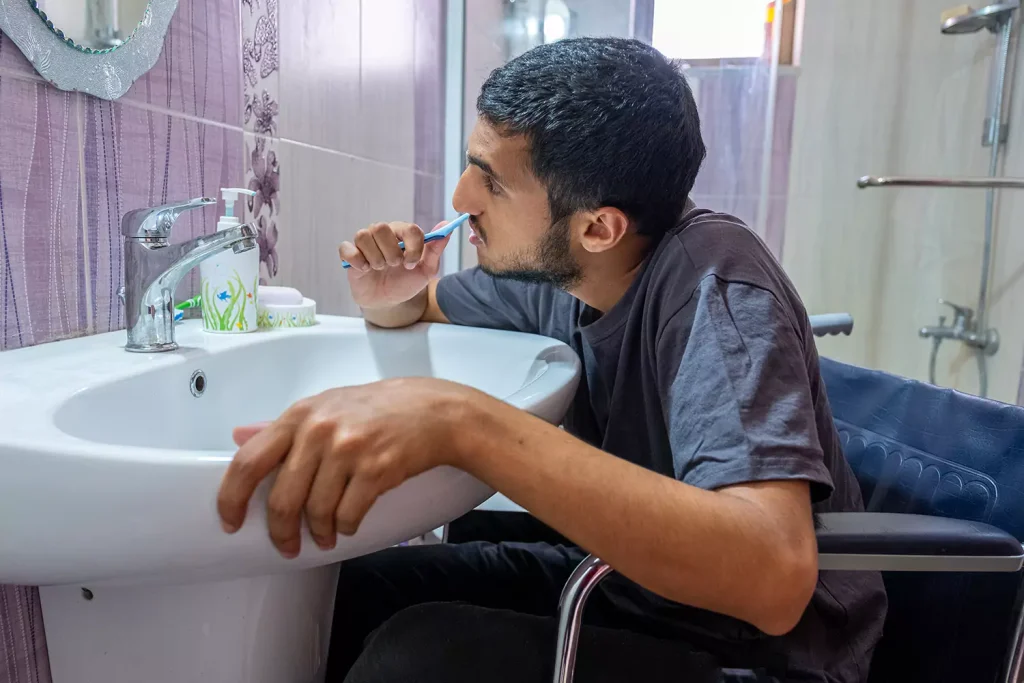 Disabled man in wheelchair brushing teeth in bathroom