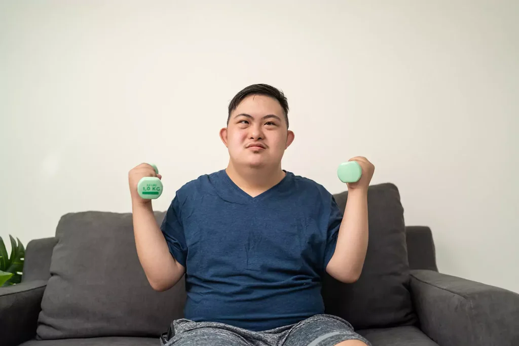 Disabled man with down syndrome sitting on couch and holding hand weights