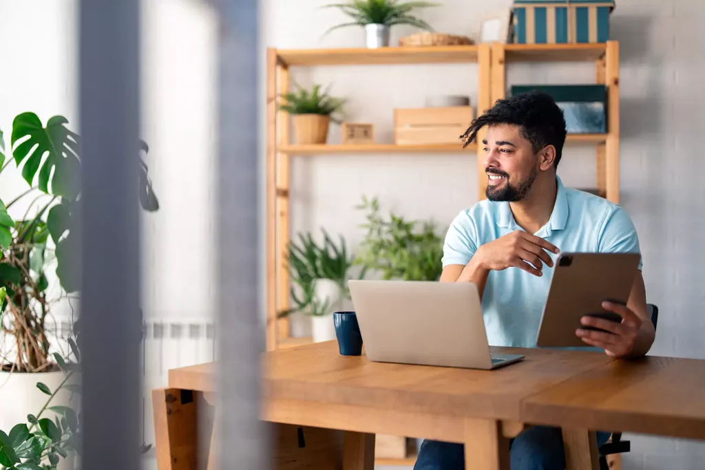 Support Coordinator holding iPad and sitting in front of laptop, looking to his right