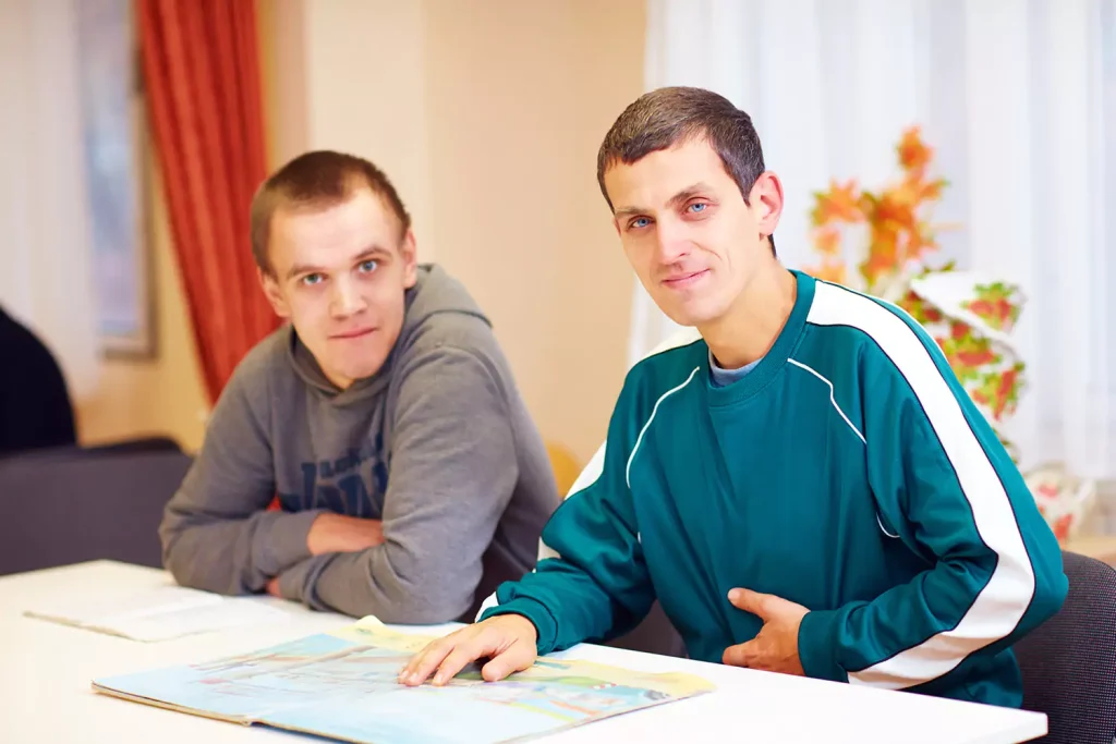 Two disabled friends reading a book and smiling at camera